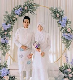 two people standing next to each other in front of a floral arch with blue and white flowers