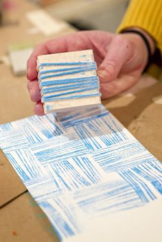 someone is making something out of paper with blue and white lines on it, while another person holds the piece of cardboard in their hand