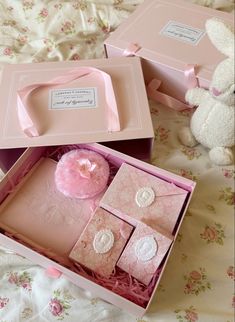 two pink boxes are open and sitting on a floral bed spread with a teddy bear