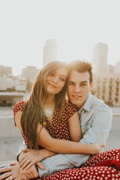 a young man and woman hugging each other in front of a cityscape with the sun shining on them