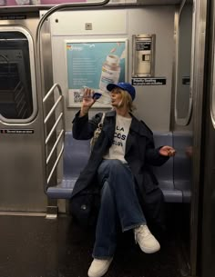 a person sitting on a subway train drinking from a water bottle and wearing a blue hat