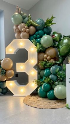 the number three is surrounded by balloons and greenery, with lights strung from it