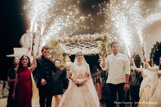 the bride and groom are walking down the aisle with sparklers in the air behind them