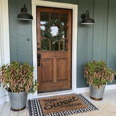 two potted plants sit on the front porch next to a welcome mat that says home sweet