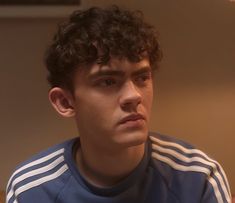 a young man with curly hair wearing a blue and white shirt looking at the camera