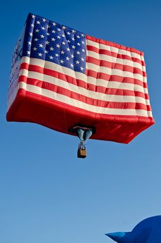 an american flag kite is flying in the sky with blue skies behind it and a large balloon