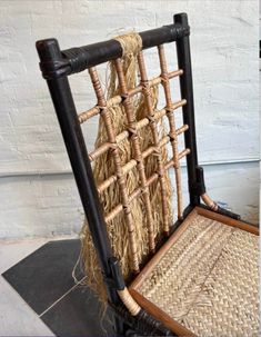 an old chair made out of straw and wood with rope on the back, sitting in front of a white wall