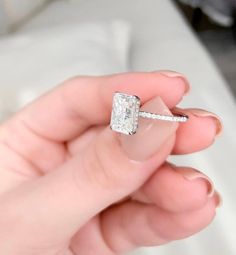 a person holding a ring with a princess cut diamond in it's middle finger