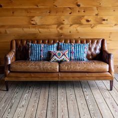 a brown leather couch sitting on top of a wooden floor next to a wooden wall