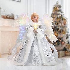 an angel figurine holding a lit candle in front of a decorated christmas tree