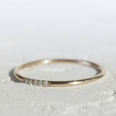 a gold wedding band with three diamonds on it, sitting on a concrete surface in front of a white background