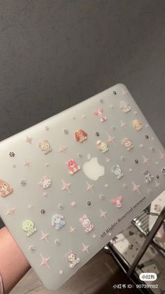 a person holding an apple laptop with many stickers on the cover and in front of them