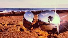 two people are reflected in sunglasses on the beach