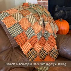 an orange and black plaid blanket sitting on top of a brown leather couch next to a fireplace