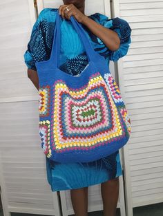 a woman holding a crocheted bag in front of her face and looking at the camera