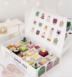 a box filled with lots of different types of cakes on top of a white table