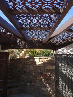 an outdoor area with a stone wall and metal lattice design on the roof above it