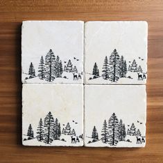 four black and white coasters with animals in the woods, on top of a wooden table