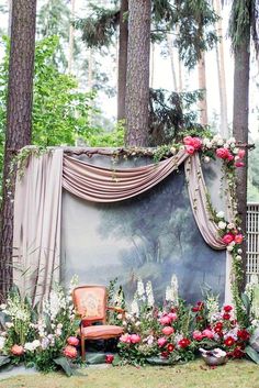 a chair sitting in the middle of a forest filled with flowers and greenery next to a painting