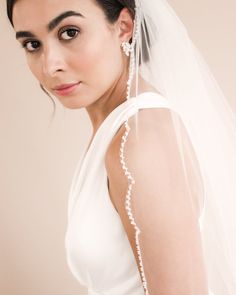 a woman wearing a wedding veil with pearls on the back of her head and shoulder