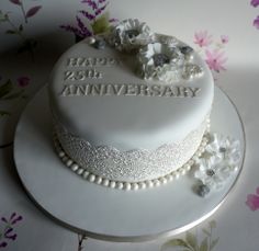 a white wedding cake with flowers and pearls on the top is decorated with an inscription happy 25th anniversary