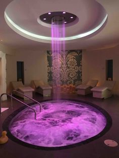 an indoor hot tub is lit up with purple lights and water in the middle of it