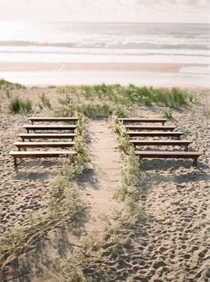 a row of wooden benches sitting on top of a sandy beach next to the ocean