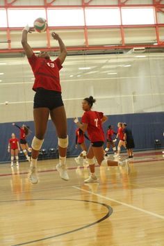 a group of girls playing volleyball in a gym with one jumping up to hit the ball