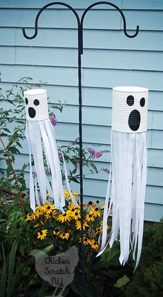 two paper cups with faces on them sitting in front of a flower pot filled with yellow flowers