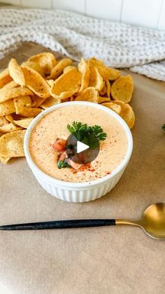 a bowl of dip next to some chips on a table with a spoon and fork