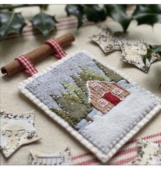 an embroidered christmas ornament on a table with holly leaves and other decorations around it