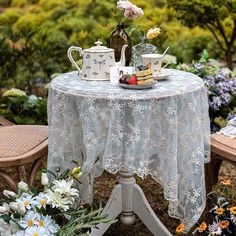 a table with two teapots on it and flowers in the foreground next to some chairs