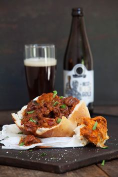 a sandwich with meat and sauce on it next to a glass of beer