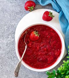 two strawberries sit on top of a bowl of strawberry jam with a spoon in it