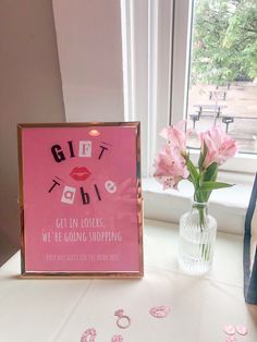 a pink sign sitting on top of a table next to a vase filled with flowers