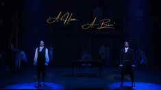 two men in vests standing on stage with the words all at once written above them