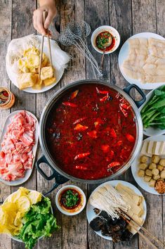 a large pot filled with lots of food on top of a wooden table next to plates and bowls