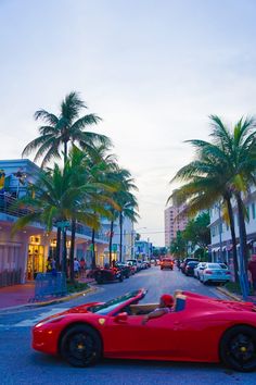 a red sports car driving down a street with palm trees in the foreground and buildings on both sides