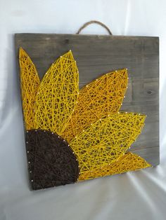 a string art sunflower is hanging on a wooden board with brown and yellow yarn