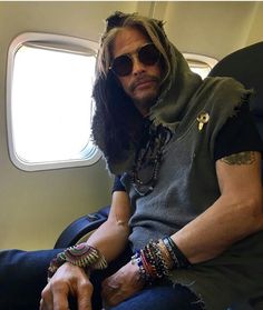 a man with long hair and sunglasses sitting on an airplane