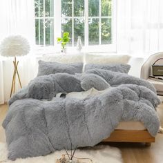 a bed covered in grey fluffy blankets next to a window