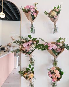 four vases with flowers hanging from the wall in front of a counter and mirror