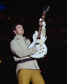 a man holding a white electric guitar in his right hand and looking up at the sky