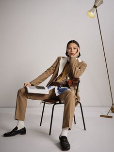 a woman sitting in a chair next to a floor lamp and holding a book with her right hand