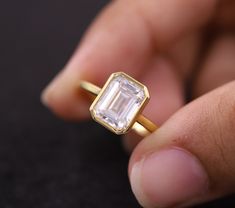 a close up of a person's hand holding a gold ring with an emerald stone