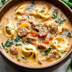 a bowl filled with pasta, meat and spinach soup on top of a table