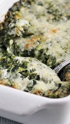 spinach and cheese casserole in a white dish with a silver serving spoon