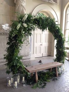 a wooden bench covered in greenery next to a white door with candles on it