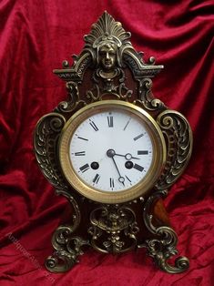 an ornate gold clock with roman numerals on a red velvet background is shown