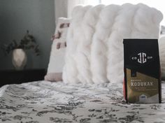 a package of coffee sitting on top of a bed next to a white blanket and pillows